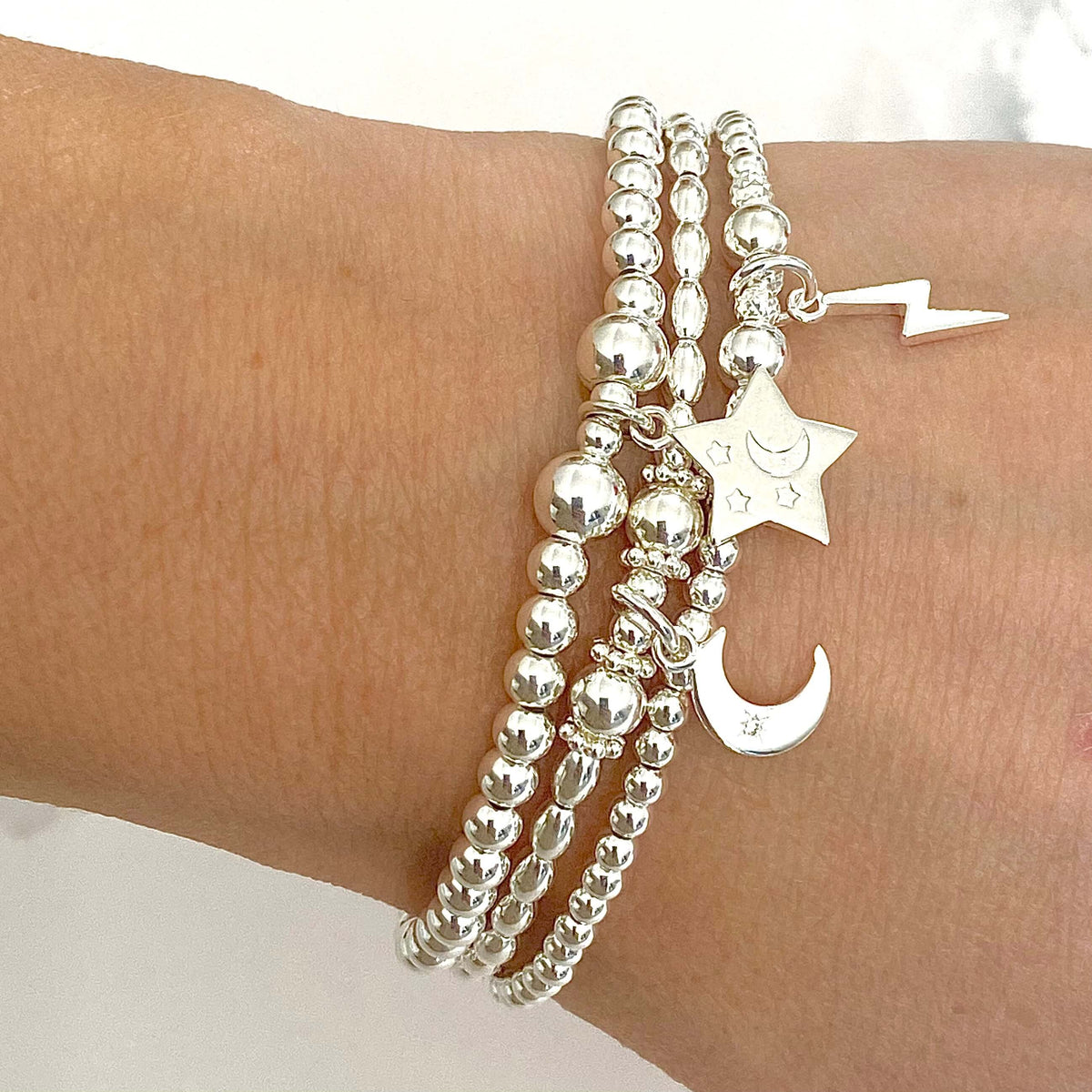 Silver beaded bracelet with star, moon and lightening charms on a wrist against a white background