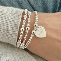 Silver beaded bracelets on a wrist with one bracelet featuring a heart-shaped charm with the word Daughter engraved on it with a tiny heart charm.