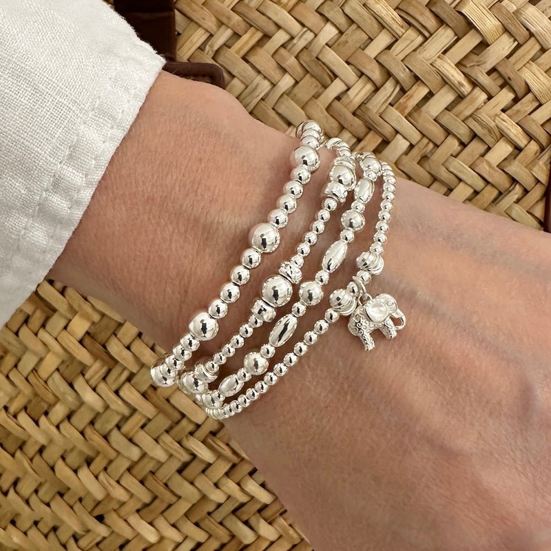 A lady's wrist wearing silver beaded bracelets, one featuring a silver elephant charm, against a woven background