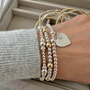 Close-up of a hand wearing multiple beaded bracelets, with one featuring a heart shaped silver charm with a tiny family tree and words 'Family is everything' engraved on the front