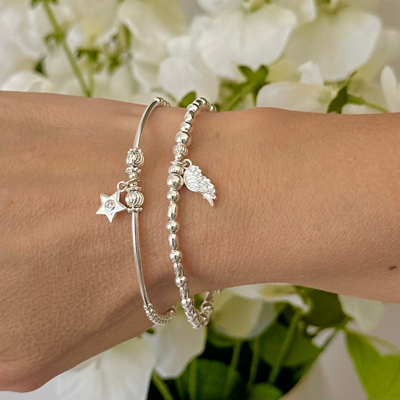 A wrist wearing two silver beaded bracelets with an angel wing and sparkly star charms