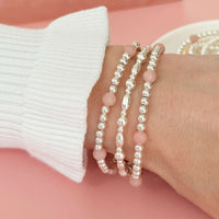 Sterling silver and pink opal beaded stacking bracelets on a wrist against a pink background