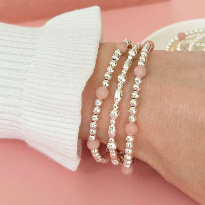 Sterling silver and pink opal beaded stacking bracelets on a wrist against a pink background