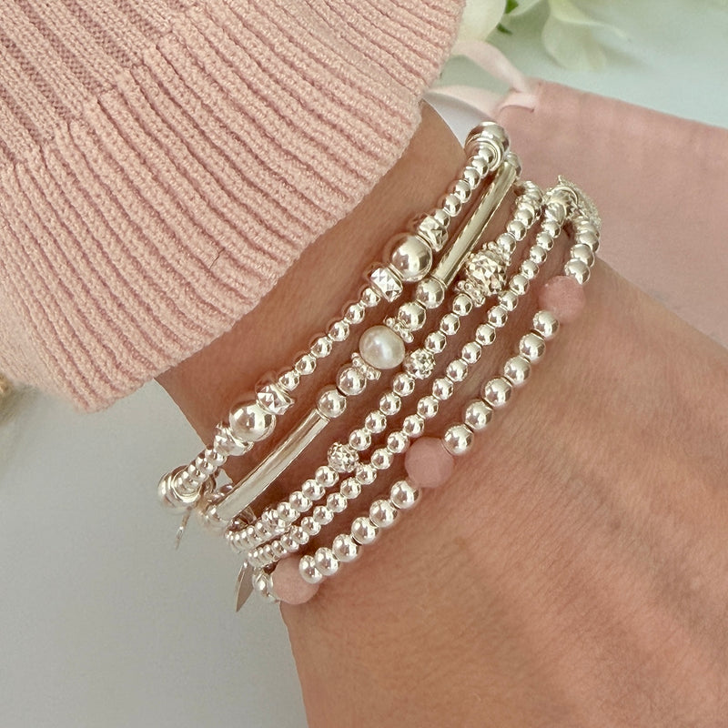 Multiple silver beaded bracelets on a wrist with a light background