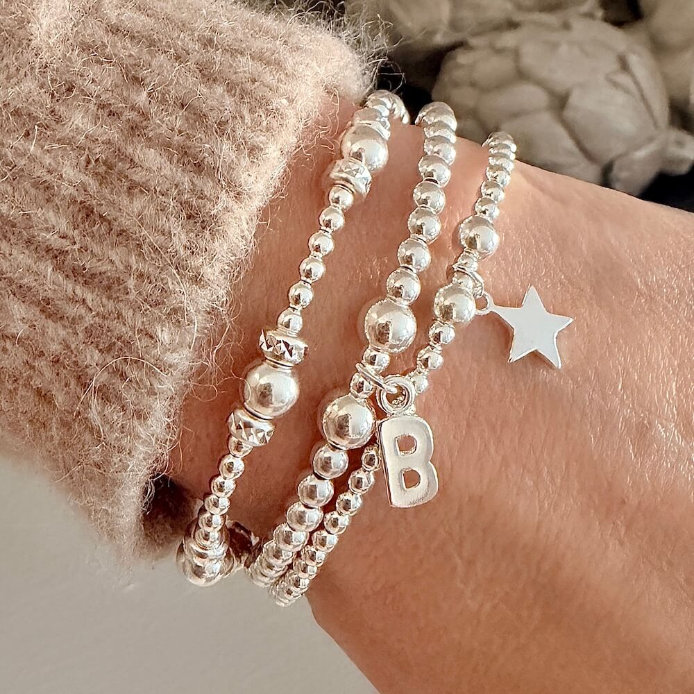 Silver beaded bracelet with a star and initial 'B' charms on a wrist.