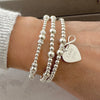 Silver beaded bracelets on a wrist with a heart-shaped 'Love you' charm with infinity charm sitting on top.