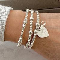 Silver beaded bracelets on a wrist with a heart-shaped 'Love you' charm with infinity charm sitting on top.