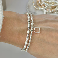Silver beaded bracelet duo with an open style studded four leaf clover on a wrist, with blurred jewellery in the background.