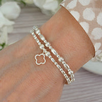 Two sterling silver beaded bracelets, one  with a clover charm on a wrist against a neutral background