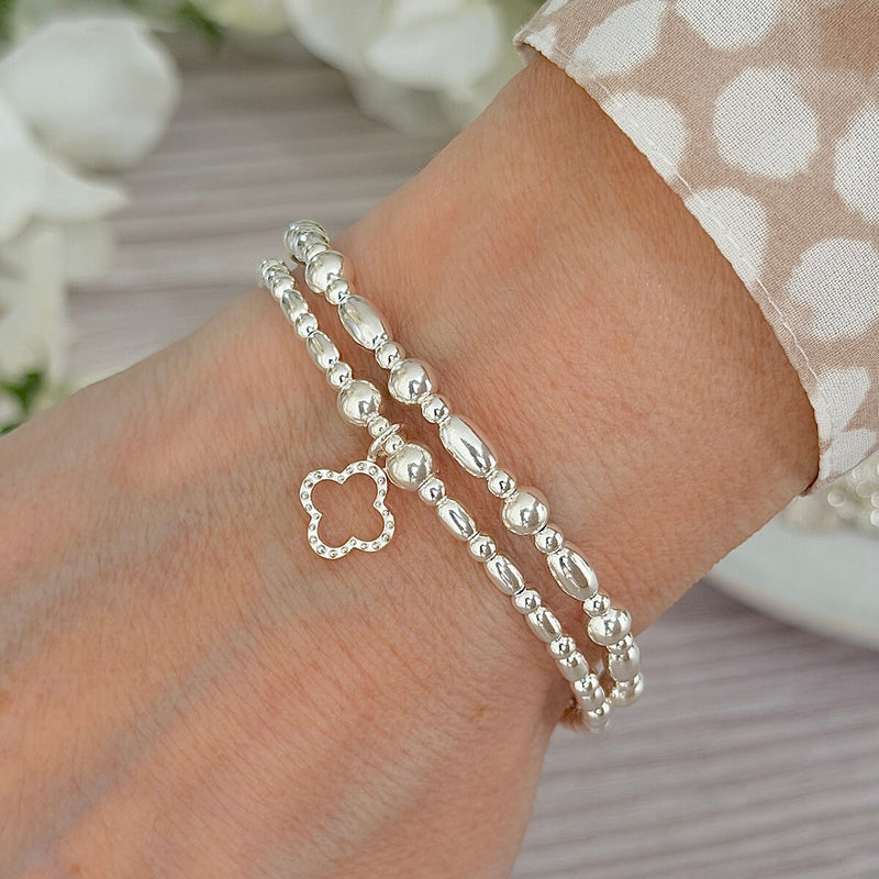 Two sterling silver beaded bracelets, one  with a clover charm on a wrist against a neutral background