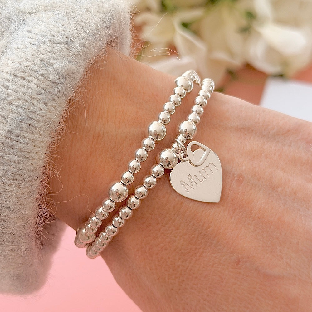 Silver beaded bracelet duo with a heart-shaped 'Mum' charm on a wrist.