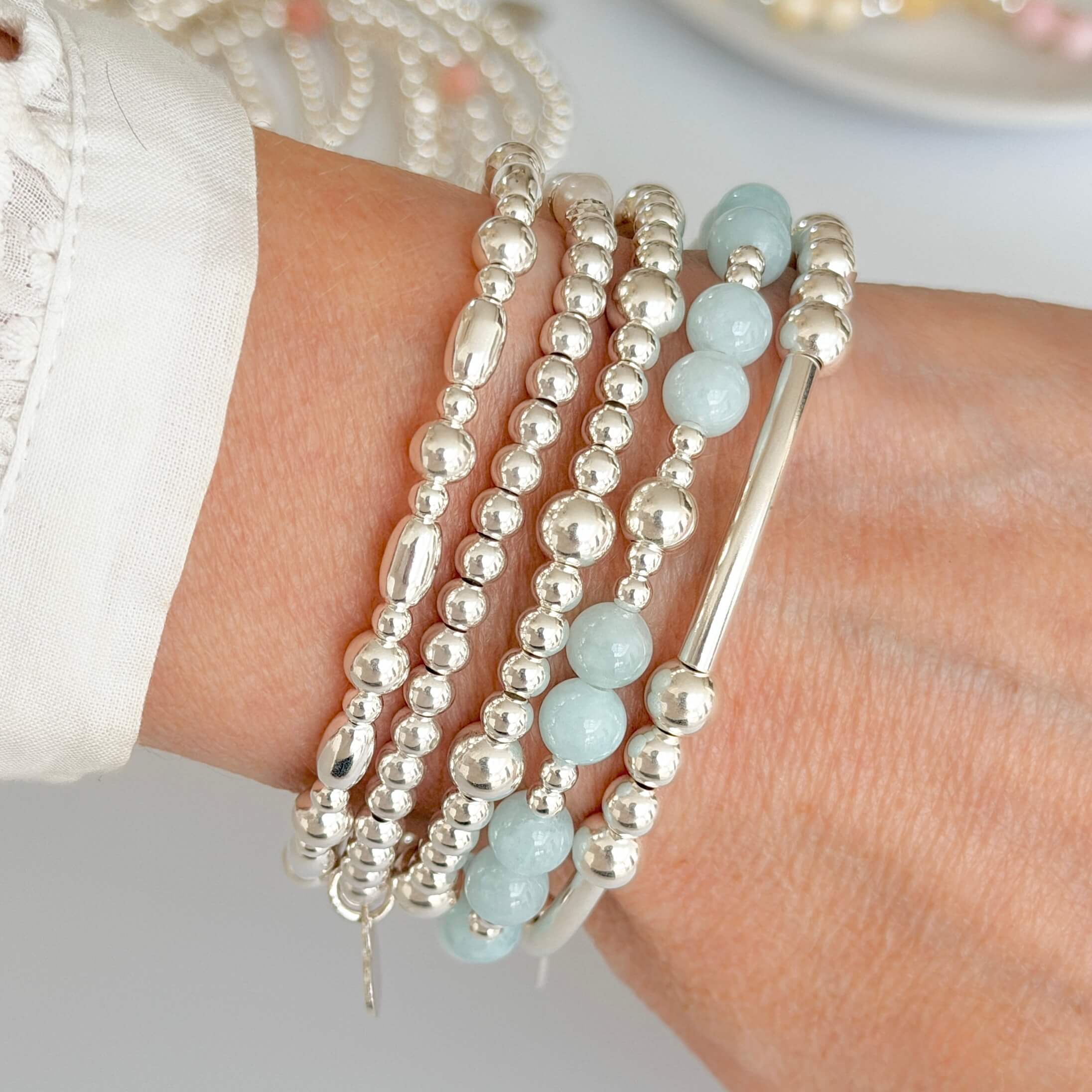 Close-up of a wrist wearing multiple beaded bracelets, one with pale blue jade and sterling silver beads, on a neutral background