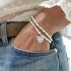 A close up of a woman's wrist wearing a Silver beaded stacking bracelet duo with one bracelet featuring a paw print heart charm, wearing a white blouse and blue jeans.