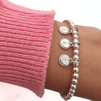 Silver bracelet with 3 engraved initial disc charms on a wrist against a pink sweater background