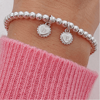 Silver beaded bracelet with letter charms on a wrist, wearing a pink sweater.