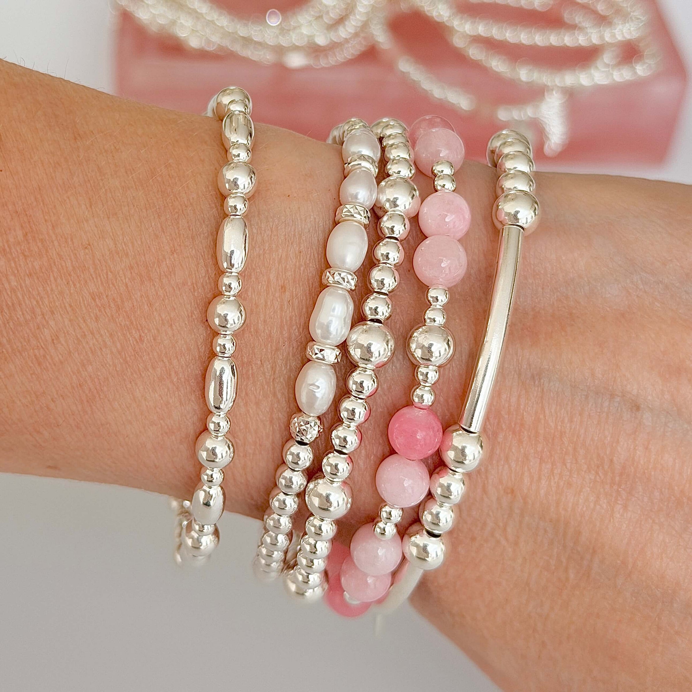 Stack of sterling silver and pink beaded bracelets on a wrist with a blurred background