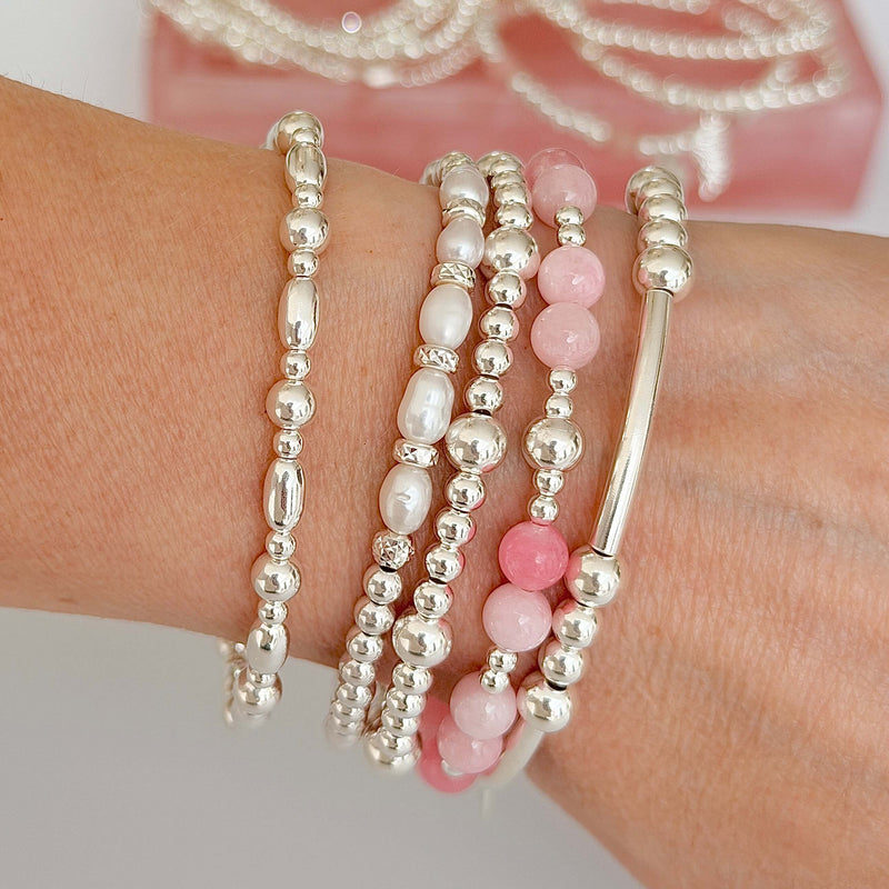 Stack of sterling silver and pink beaded bracelets on a wrist with a blurred background