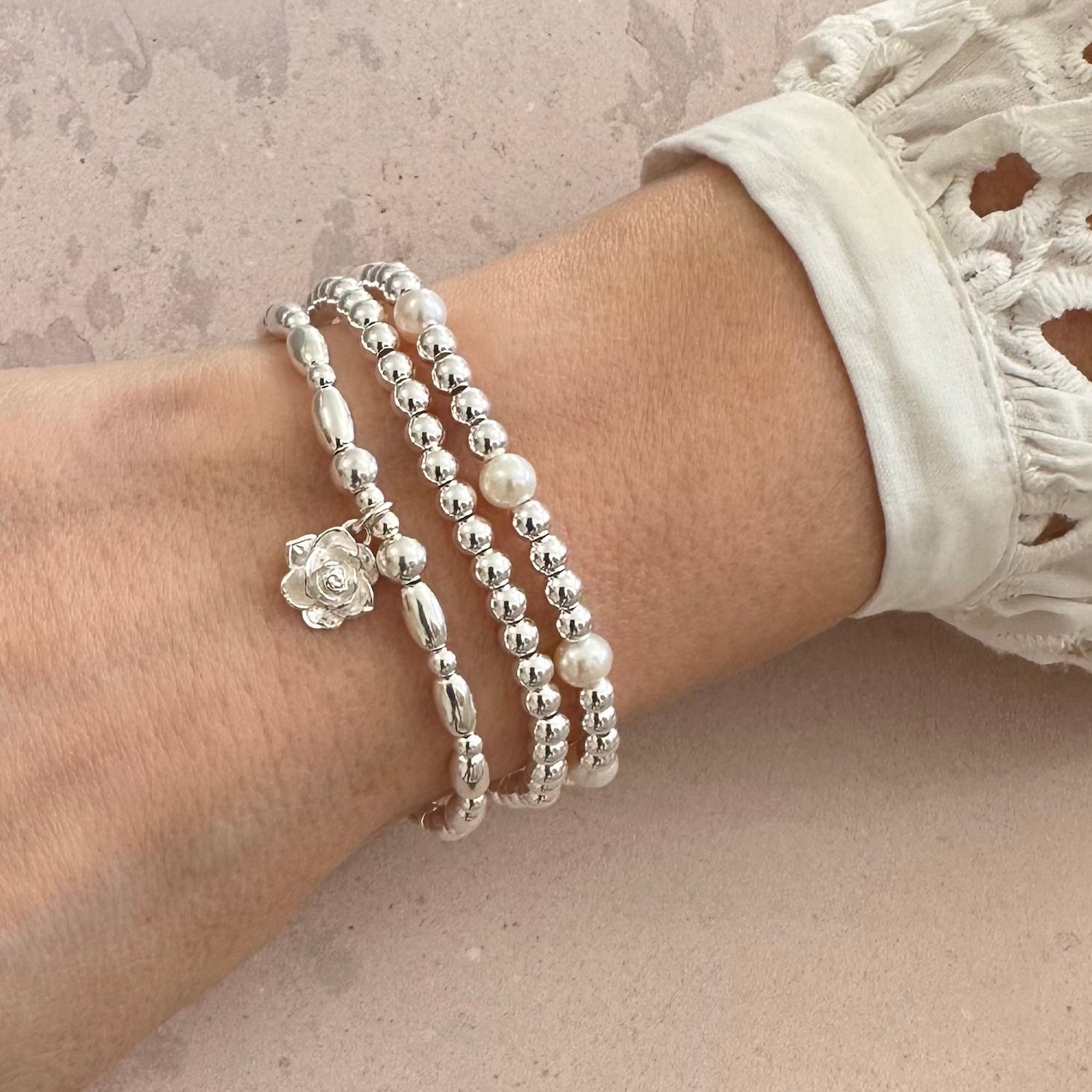 Silver beaded bracelets, one featuring as silver flower charm, on a wrist against a neutral background