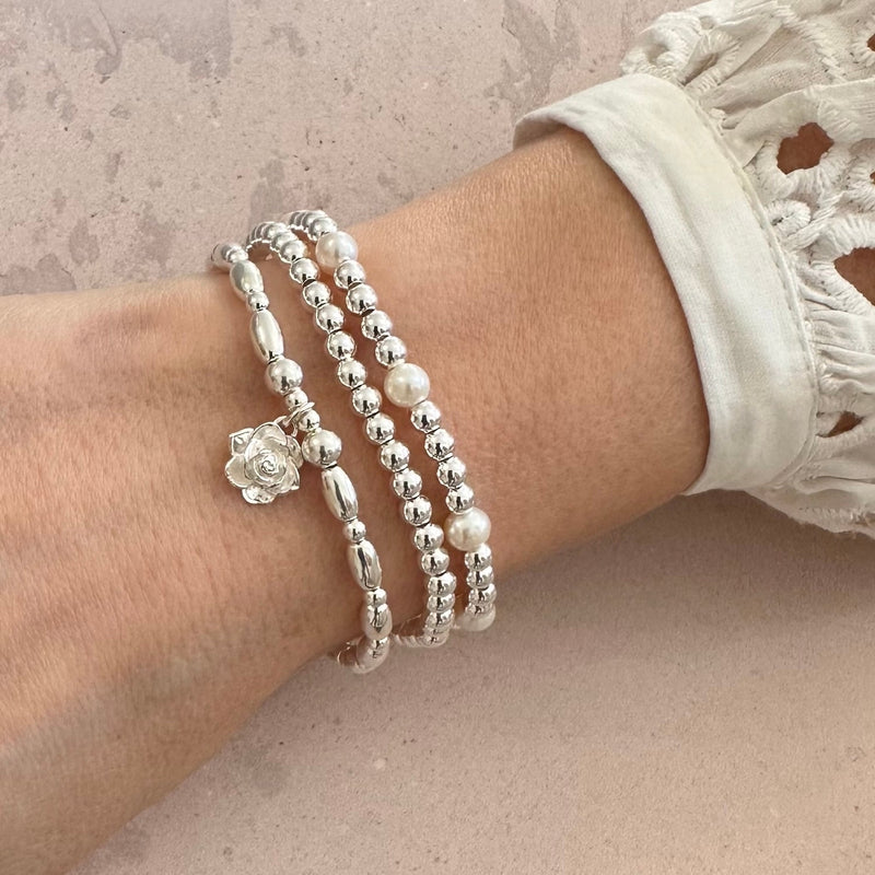 Silver beaded bracelets, one featuring as silver flower charm, on a wrist against a neutral background