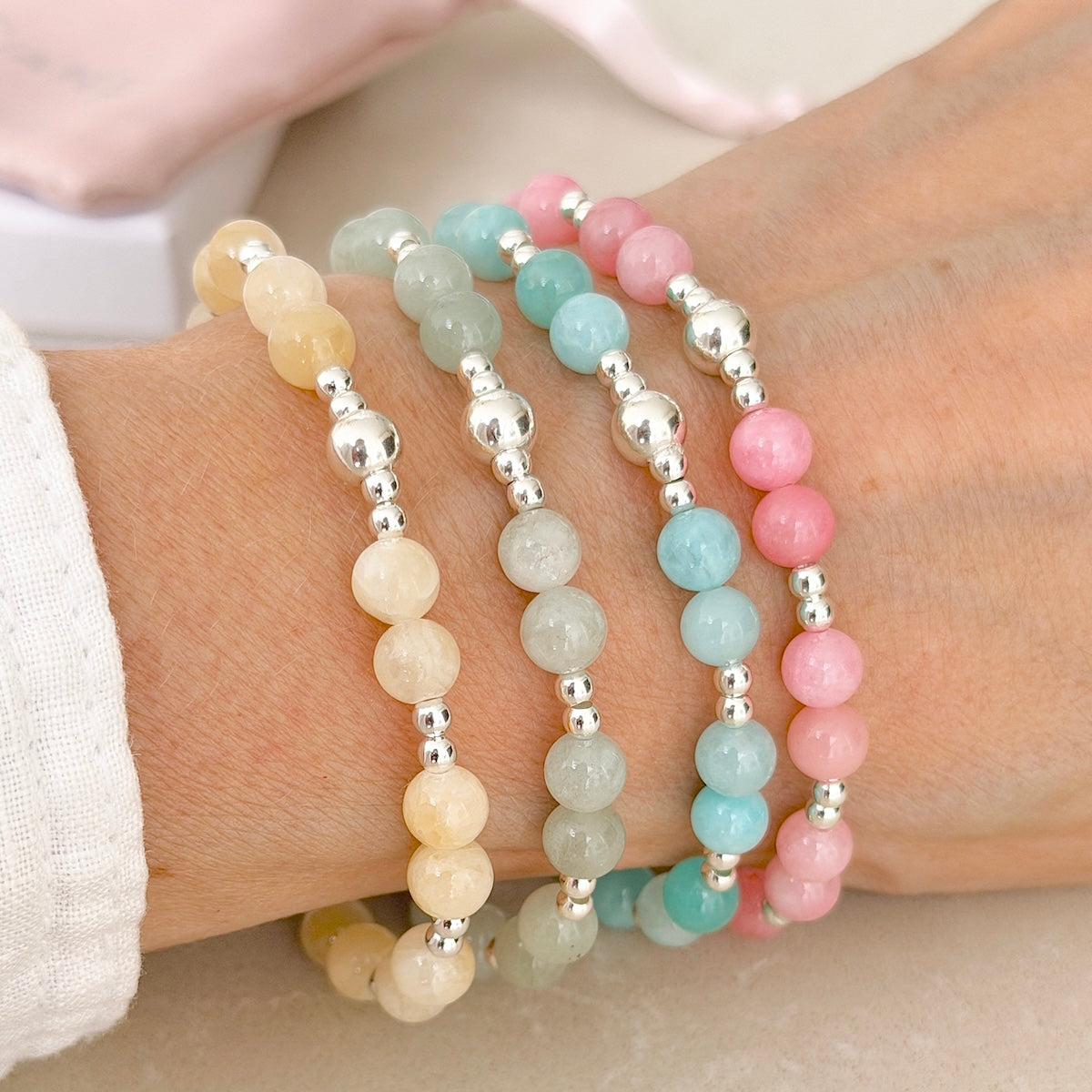 Four pastel coloured and sterling silver beaded bracelets  on a wrist against a neutral background.