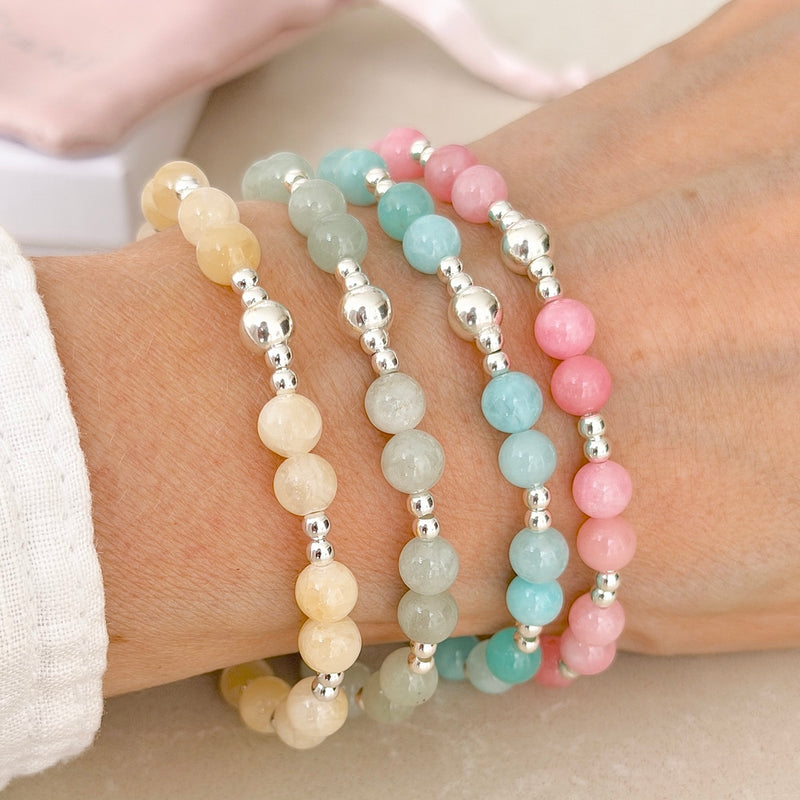 Four pastel coloured and sterling silver beaded bracelets  on a wrist against a neutral background.