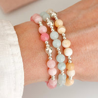 Three summer beaded sterling silver stacking bracelets with pink, blue, and yellow beads on a wrist against a neutral background