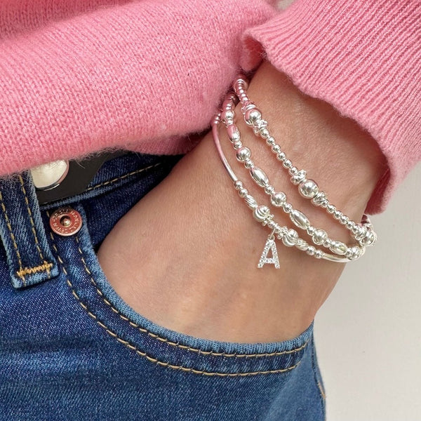 Silver bracelet with letter 'A' charm on wrist wearing pink sweater and blue jeans.