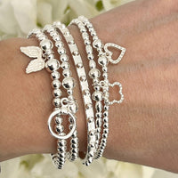 Silver bracelets with various charms on a wrist against a blurred floral background