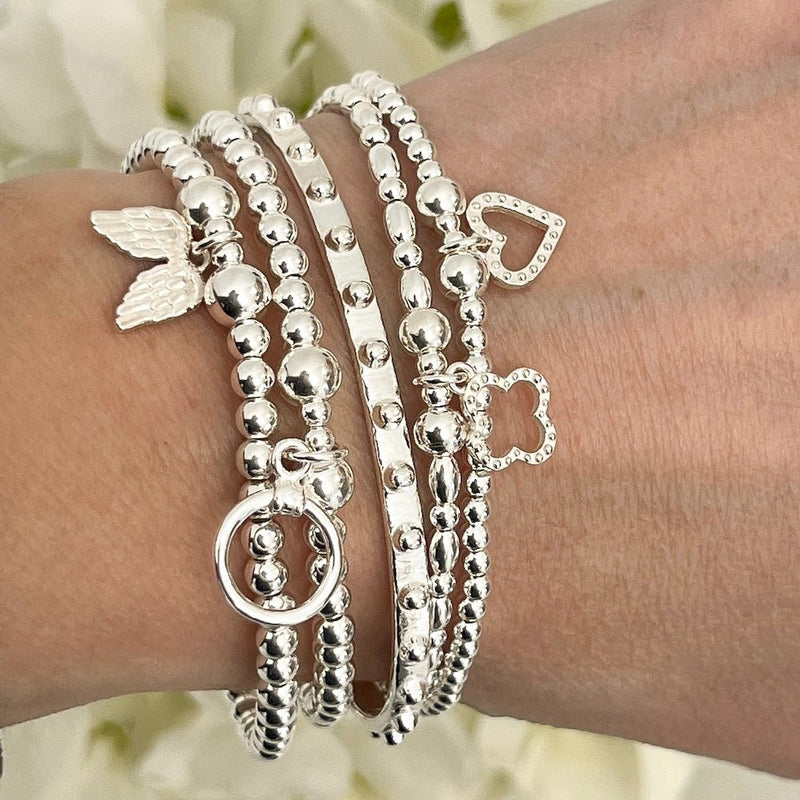 Silver bracelets with various charms on a wrist against a blurred floral background