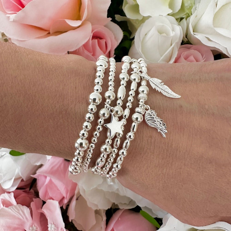 Silver bracelets with charms on a wrist against a floral background