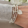 Silver beaded bracelet with a heart-shaped charm with the words 'You've Got This' engraved and a tiny open heart charm sitting on top of it. Worn on a wrist with two other beaded stacking bracelets, against a neutral background.