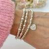 A close up image of a woman's wrist wearing 3 silver beaded stacking bracelets with one bracelet featuring a silver heart charm with the angel number 1111 on the charm
