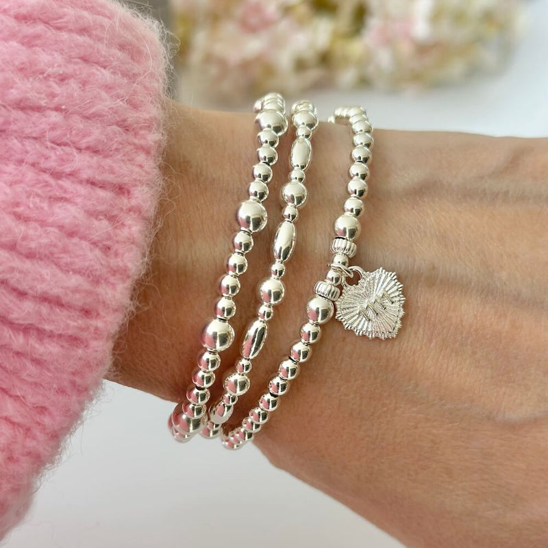 A close up image of a woman's wrist wearing 3 silver beaded stacking bracelets with one bracelet featuring a silver heart charm with the angel number 1111 on the charm