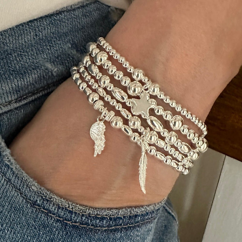 Silver Bella Jane bracelets with charms on a wrist, wearing blue jeans.