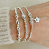 3 silver beaded stacking bracelets, one featuring a small star charm with a tiny cubic zirconia stone in centre of the charm, on a wrist against a neutral background