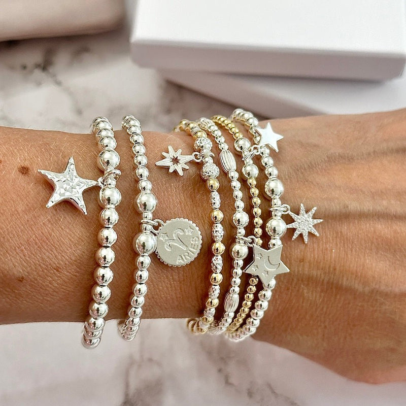 Multiple sterling silver bracelets with star and zodiac charms on a wrist against a marble background