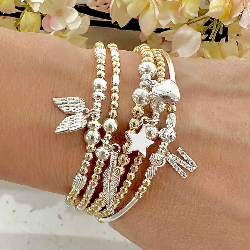 Stack of gold and silver beaded bracelets on a wrist with flowers in the background