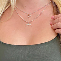 Close-up of a person wearing two necklaces with heart and t-bar pendants.