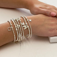 Stack of seven silver beaded stacking bracelets with charms on a wrist with a neutral background