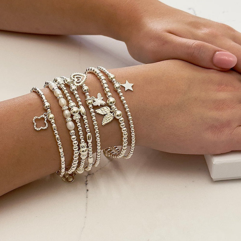 Stack of seven silver beaded stacking bracelets with charms on a wrist with a neutral background