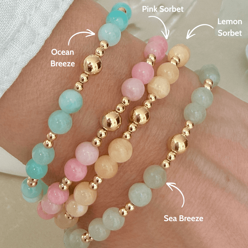 Pastel beaded bracelets with gold beads, stacked on a wrist with labelled colours.