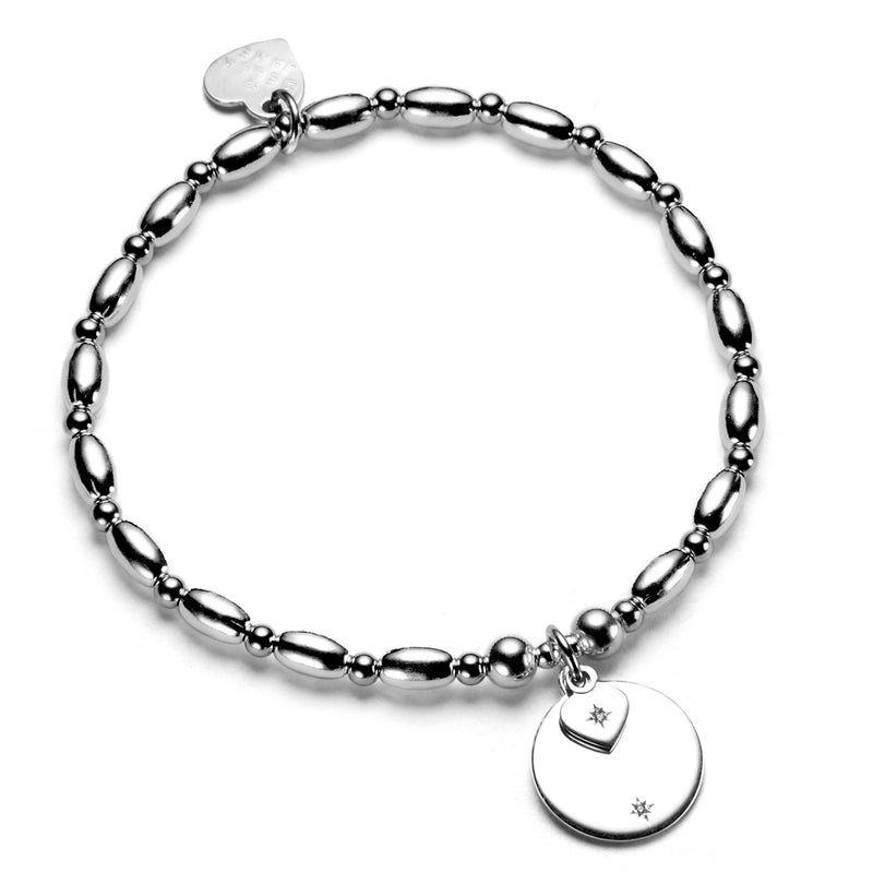 A sterling silver beaded stacking bracelet with a round disc charm and a small heart charm, featuring a subtle sparkle from the cubic zirconia.