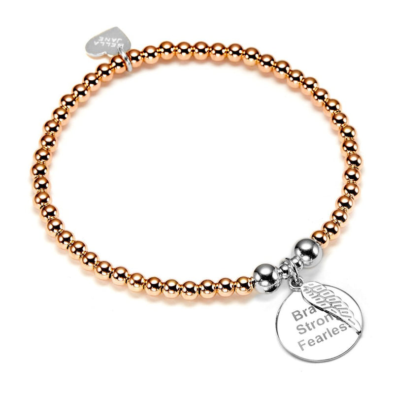 A rose gold beaded bracelet with a round silver disc charm with the words Brave, Strong, Fearless engraved on the front, with a tiny angel wing sitting on top of the disc, against a white background.
