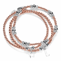 Stack of silver and rose gold mixed metal beaded bracelets with star and initial charms on a white background