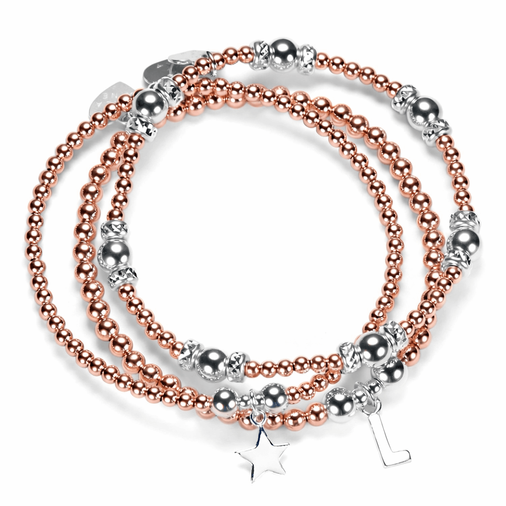 Stack of silver and rose gold mixed metal beaded bracelets with star and initial charms on a white background