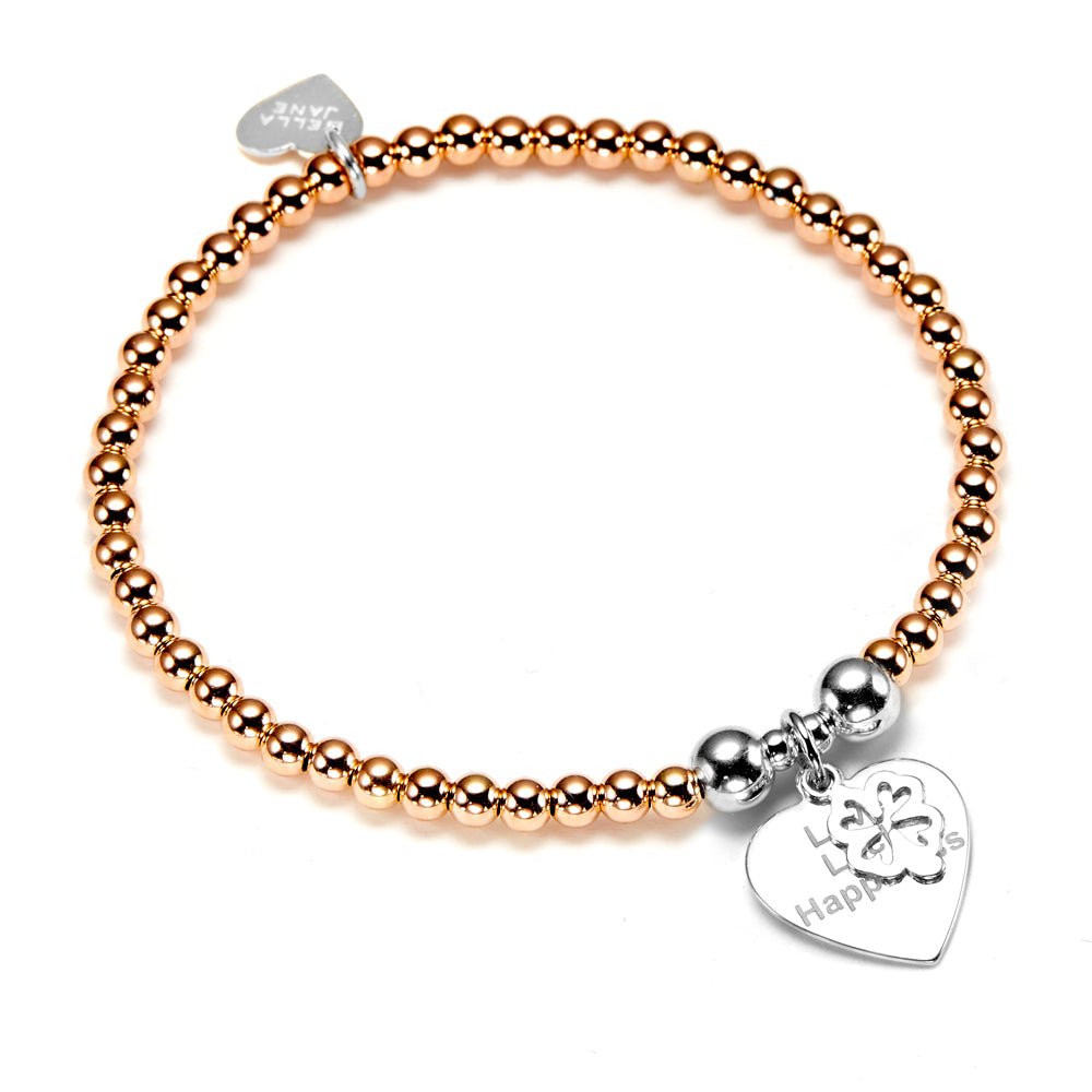 A rose gold beaded bracelet with a silver heart-shaped charm with the words 'Love Luck Happiness' engraved pictured on a white background