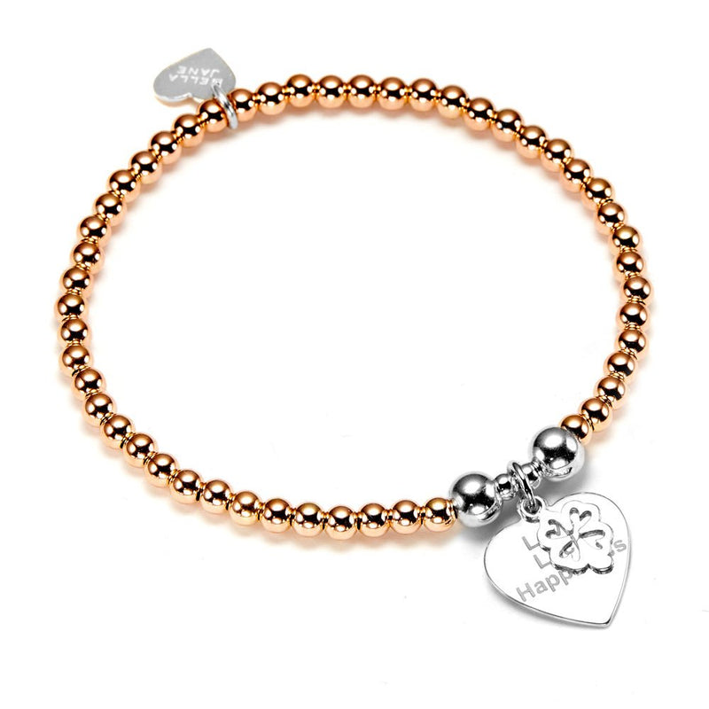 A rose gold beaded bracelet with a silver heart-shaped charm with the words 'Love Luck Happiness' engraved pictured on a white background