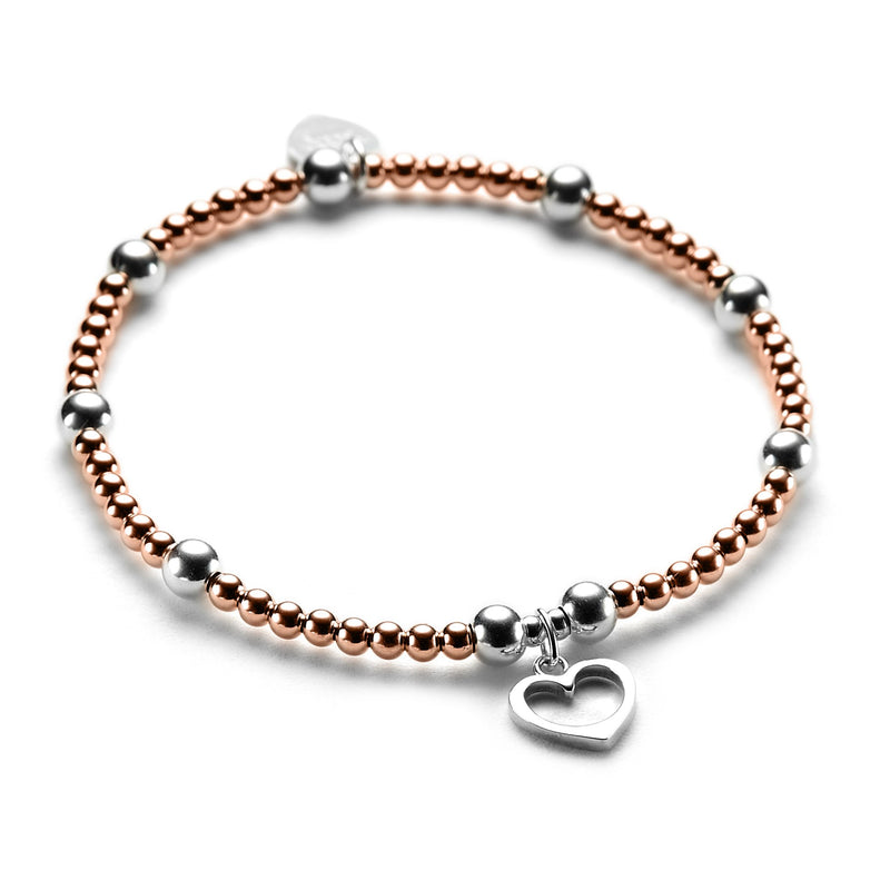 Rose gold and sterling silver beaded bracelet featuring a silver open heart charm on a white background