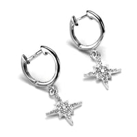 A pair of sterling silver huggie earrings with cubic zirconia starburst charms dangling from them.
