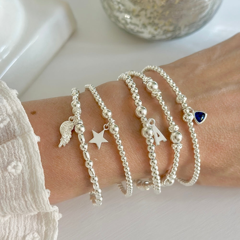 Silver bracelets with various charms on a wrist against a neutral background